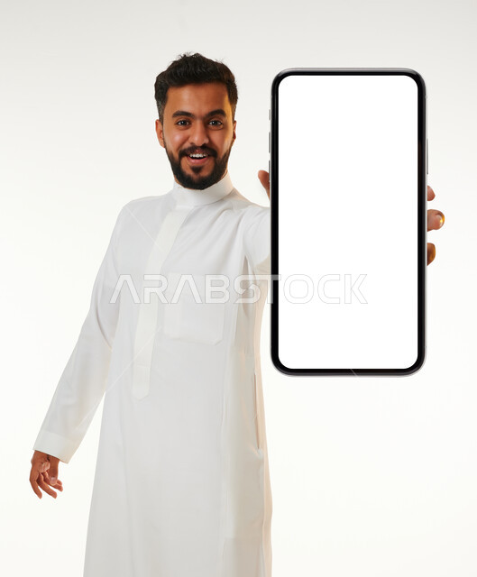 بورتريه لشاب عربي خليجي سعودي يقوم بعرض جهاز الهاتف المحمول بإيماءات مختلفة ، الحصول على الهدف المراد ، التسويق الرقمي ، اعلانات تسويقية ترويجية ، تطبيقات الهاتف الذكي , استخدام التقنية الحديثة , خلفية بيضاء .