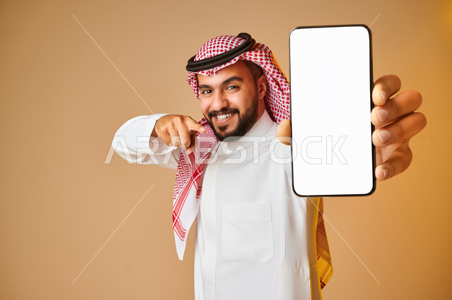 بورتريه لشاب عربي خليجي سعودي يقوم بعرض جهاز الهاتف المحمول بإيماءات مختلفة ، الحصول على الهدف المراد ، التسويق الرقمي ، اعلانات تسويقية ترويجية ، تطبيقات الهاتف الذكي , استخدام التقنية الحديثة , خلفية بنية .