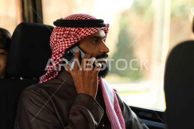 رجل عربي خليجي سعودي يجلس في إحدى وسائل النقل العامه, إجراء مكالمه هاتفيه عبر الهاتف المحمول, رحله ممتعه، نزهه في الهواء الطلق, التنقل في وسائل المواصلات, جوله سياحيه