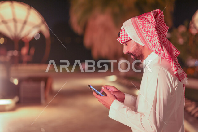 رجل عربي خليجي سعودي يستخدم الهاتف المحمول، تصفح الإنترنت، التواصل مع الأصدقاء، إستخدام وسائل التواصل الإجتماعي، هاتف محمول، استخدام تقنيات حديثة، دردشة الكترونية، منتزهات وحدائق