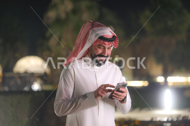رجل عربي خليجي سعودي يستخدم الهاتف المحمول، تصفح الإنترنت، التواصل مع الأصدقاء، إستخدام وسائل التواصل الإجتماعي، هاتف محمول، استخدام تقنيات حديثة، دردشة الكترونية، منتزهات وحدائق