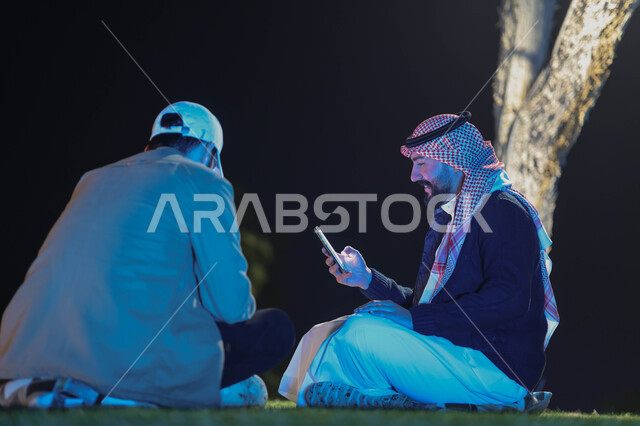 Two Saudi Arabian Gulf youth spending fun times, using mobile phones, youth session, youth friendships, discussions and dialogues, parks and gardens
