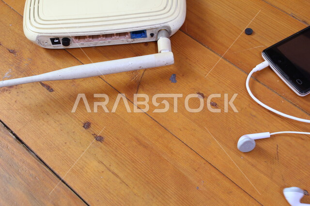 صورة مقربة لهاتف محمول مع سماعات الاذن، سماعات سلكية، موجه شبكات، جهاز الواي فاي، اجهزة تقنية حديثة، هاتف محمول، اجهزة شبكية، طاولة خشبية
