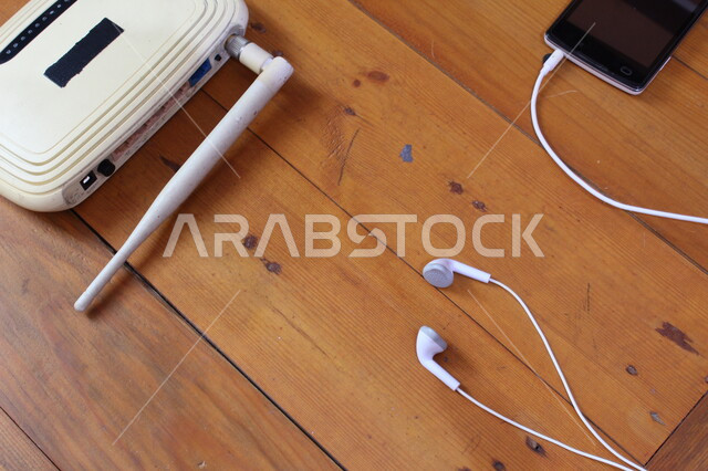 صورة مقربة لهاتف محمول مع سماعات الاذن، سماعات سلكية، موجه شبكات، جهاز الواي فاي، اجهزة تقنية حديثة، هاتف محمول، اجهزة شبكية، طاولة خشبية