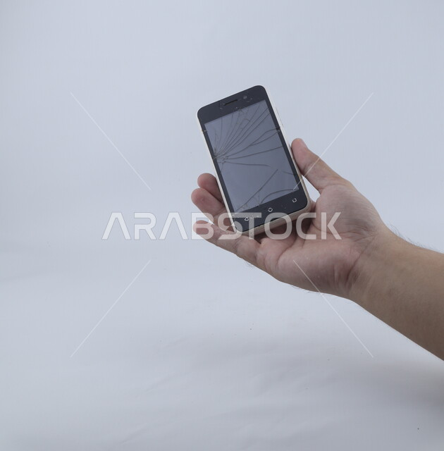 يد تحمل الهاتف المحمول ، الهاتف الخلوي بشاشة مكسورة ، خلفية بيضاء