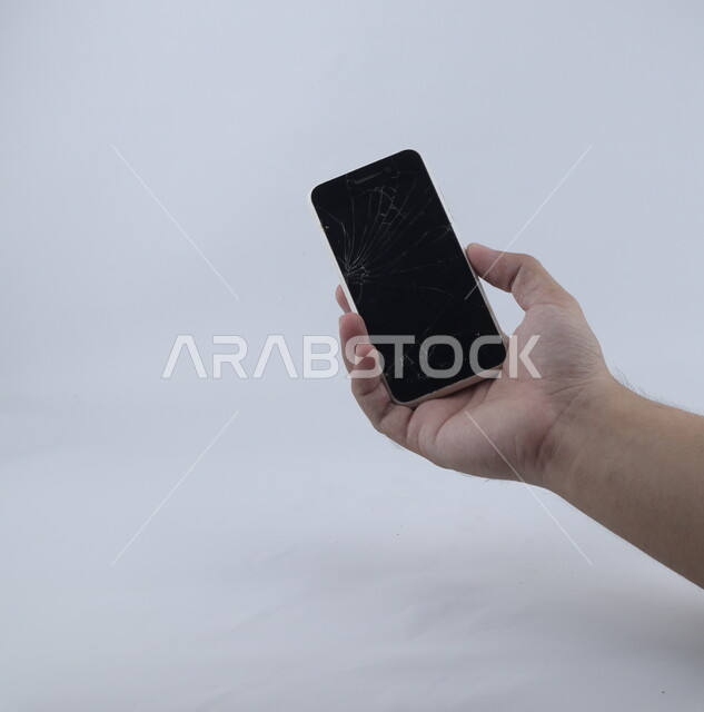 يد تحمل الهاتف المحمول ، الهاتف الخلوي بشاشة مكسورة ، خلفية بيضاء