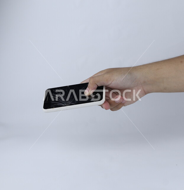 يد تحمل الهاتف المحمول ، الهاتف الخلوي بشاشة مكسورة ، خلفية بيضاء