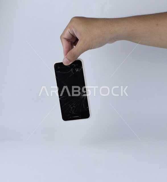 يد تحمل الهاتف المحمول ، الهاتف الخلوي بشاشة مكسورة ، خلفية بيضاء