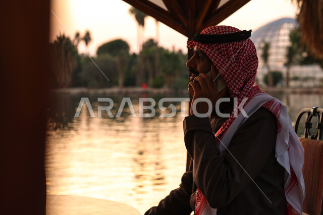رجل عربي خليجي سعودي يقضي اوقات ممتعة في احد الاماكن السياحية الترفيهية، استخدام الهاتف المحمول، اجراء مكالمة هاتفية، دردشة مع الأصدقاء، بركة مائية، أنشطة ترفيهية، نزهه في الهواء الطلق