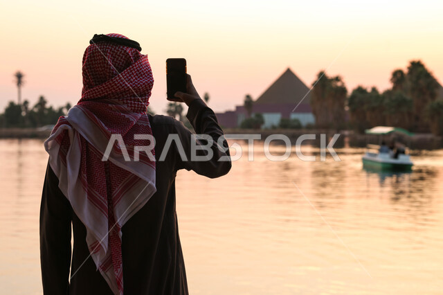 رجل عربي خليجي سعودي يقضي اوقات ممتعة في احد الاماكن السياحية الترفيهية، استخدام الهاتف المحمول، التقاط صور تذكارية، بث مباشر، بركة مائية، أنشطة ترفيهية، نزهه في الهواء الطلق