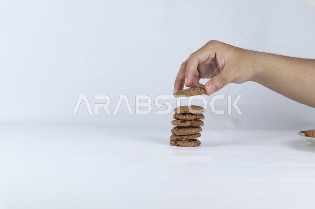 صوره مقربه ليد تأخذ حبه من رقائق البسكويت بالشوكولاته ، رقاقات البسكويت الهشة ، كوكيز ، بسكويت الشوكولاتة ، حلويات مخبوزة طازجة, خلفيه بيضاء