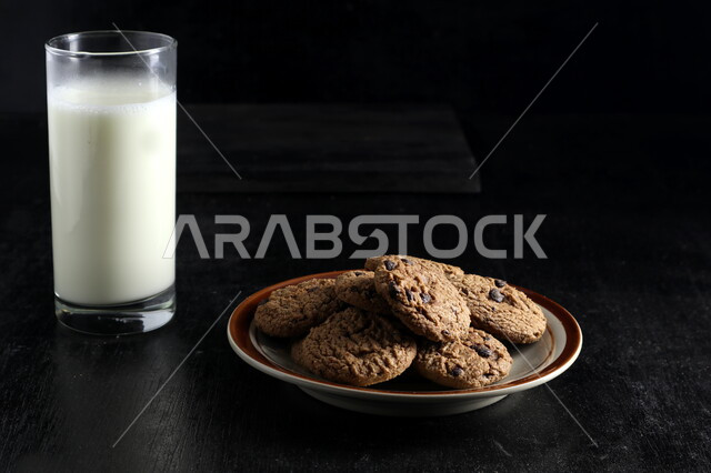 Set of chocolate chip cookies, a glass of milk, crispy biscuit chips, cookies, chocolate biscuits, freshly baked sweets, black background