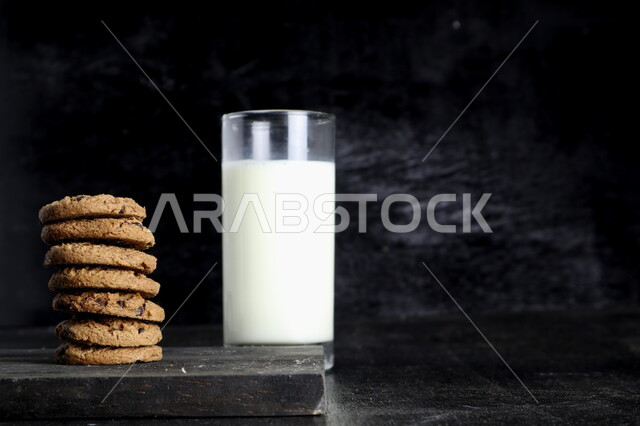 مجموعه من رقائق البسكويت بالشوكولاته ، كوب من الحليب,  رقاقات البسكويت الهشة ، كوكيز ، بسكويت الشوكولاتة ، حلويات مخبوزة طازجة, خلفيه سوداء