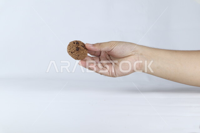 صوره مقربه ليد تمسك حبه من رقائق البسكويت بالشوكولاته ، رقاقات البسكويت الهشة ، كوكيز ، بسكويت الشوكولاتة ، حلويات مخبوزة طازجة, خلفيه بيضاء