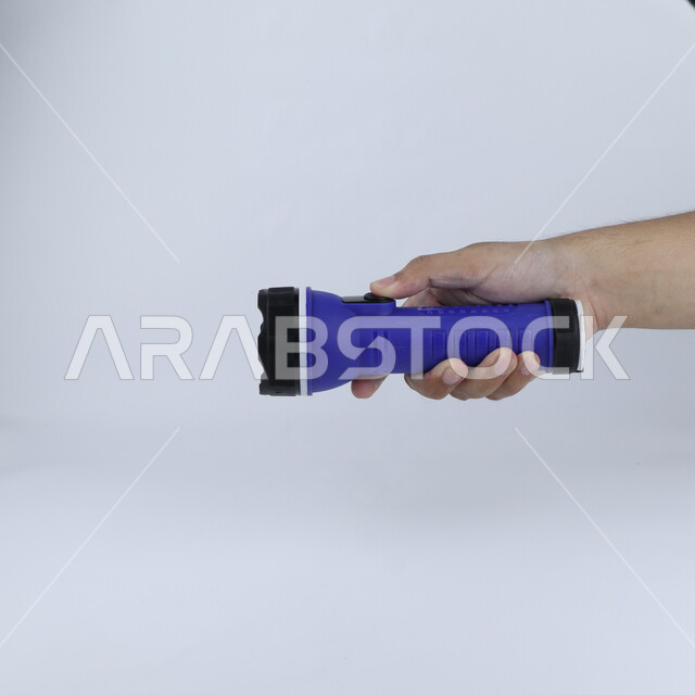 يد تحمل مصباح يدوي معزول على خلفية بيضاء ، كشاف ، المشعل الكهربائي