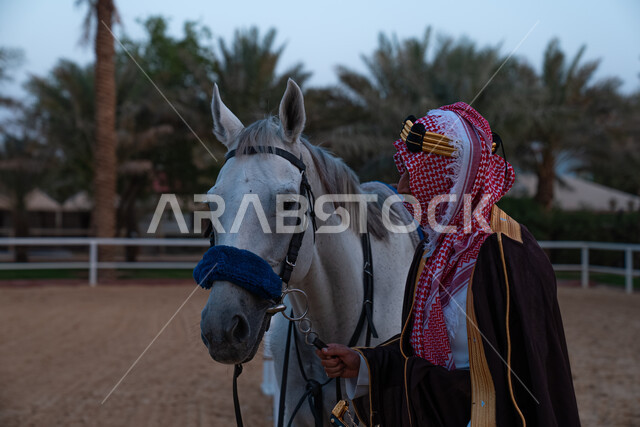 فارس عربي خليجي سعودي يرتدي زي تراثي شعبي ويقف مع الخيل، الخيل العربي الاصيل، زي شعبي للأعياد والمناسبات الوطنية، يوم التاسيس السعودي 