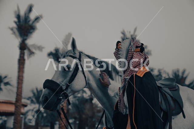 فارس عربي خليجي سعودي يرتدي زي تراثي شعبي ويقف مع الخيل، الخيل العربي الاصيل، زي شعبي للأعياد والمناسبات الوطنية، يوم التاسيس السعودي 