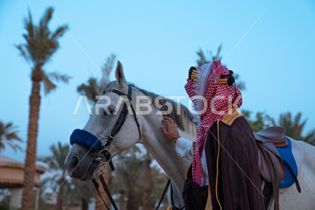 فارس عربي خليجي سعودي يرتدي زي تراثي شعبي ويقف مع الخيل، الخيل العربي الاصيل، زي شعبي للأعياد والمناسبات الوطنية، يوم التاسيس السعودي 