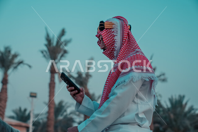 A Saudi Arabian Gulf knight wearing a traditional costume and using a mobile phone, wearing a traditional costume for national holidays and events, the day of the Saudi founding