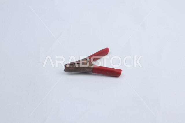 مشبك بطاريات معدني، واقي بلاستيكي احمر، كماشات صغيرة، خلفية بيضاء