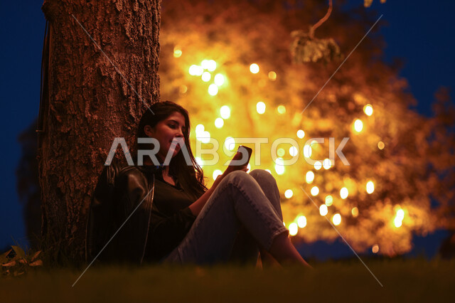 امرأة عربية خليجية سعودية تستخدم الهاتف المحمول، تصفح الإنترنت، هاتف محمول، دردشة الكترونية، استخدام تقنيات حديثة، حدائق ومنتزهات، اماكن هادئة، الجلوس في الهواء الطلق