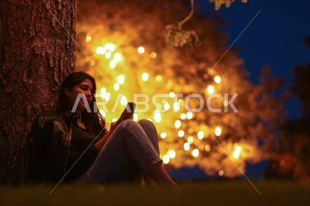 امرأة عربية خليجية سعودية تستخدم الهاتف المحمول، تصفح الإنترنت، هاتف محمول، دردشة الكترونية، استخدام تقنيات حديثة، حدائق ومنتزهات، اماكن هادئة، الجلوس في الهواء الطلق