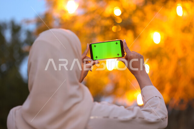 امرأة عربية خليجية سعودية تستخدم هاتف محمول بشاشة خضراء، كروما، شاشة كروما خضراء، هاتف محمول، التقاط صور تذكارية، بث مباشرة، استخدام تقنيات حديثة، نزهة في الهواء الطلق