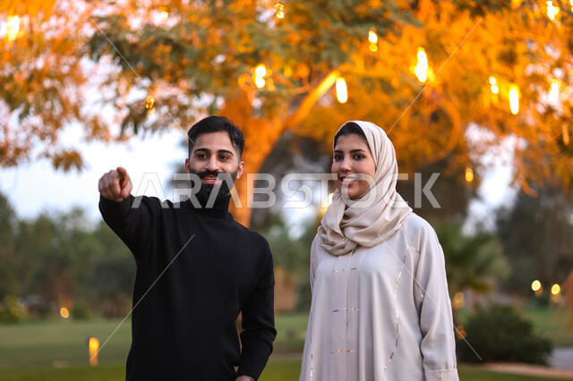 زوجان عربيان خليجيان يقضيان اوقات ممتعة في احد الحدائق العامة بالسعودية، الحدائق والمنتزهات، الطبيعة الخضراء، الاشارة نحو شيء ما، اجواء عائلية سعيدة، نزهة في الهواء الطلق