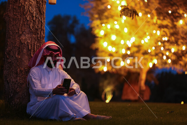 رجل عربي خليجي سعودي يستخدم الهاتف المحمول، تصفح الإنترنت، هاتف محمول، دردشة الكترونية، استخدام تقنيات حديثة، حدائق ومنتزهات، اماكن هادئة، الجلوس في الهواء الطلق