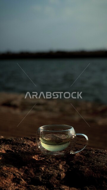 كوب زجاجي شفاف على شاطئ البحر ، خلفية ضبابية لشاطئ البحر