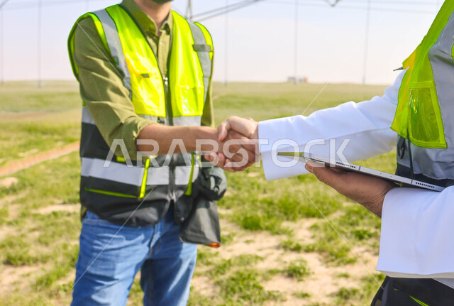 مهندسان زراعيان عربيان خليجيان سعوديان في حقل زراعي ، إرتداء خوذة وسترة الحماية، إتفاقيات و صفقات عمل، الاراضي والحقول الزراعية، آلات ومعدات الري المستقبلي، اذرع الري المحوري