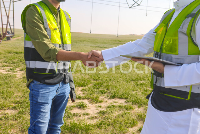 مهندسان زراعيان عربيان خليجيان سعوديان في حقل زراعي ، إرتداء خوذة وسترة الحماية، إتفاقيات و صفقات عمل، الاراضي والحقول الزراعية، آلات ومعدات الري المستقبلي، اذرع الري المحوري