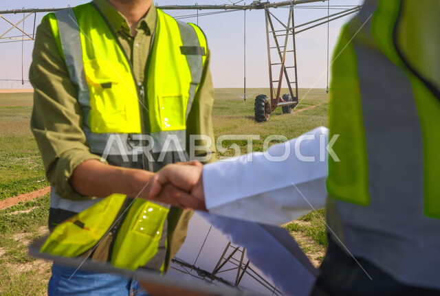 مهندسان زراعيان عربيان خليجيان سعوديان في حقل زراعي ، إرتداء خوذة وسترة الحماية، إتفاقيات و صفقات عمل، الاراضي والحقول الزراعية، آلات ومعدات الري المستقبلي، اذرع الري المحوري