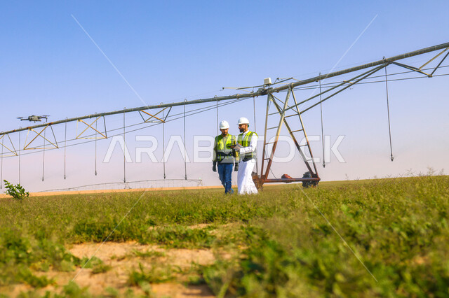 مهندسان زراعيان عربيان خليجيان سعوديان في حقل زراعي ، إرتداء خوذة وسترة الحماية، إتفاقيات و صفقات عمل، الاراضي والحقول الزراعية، آلات ومعدات الري المستقبلي، اذرع الري المحوري