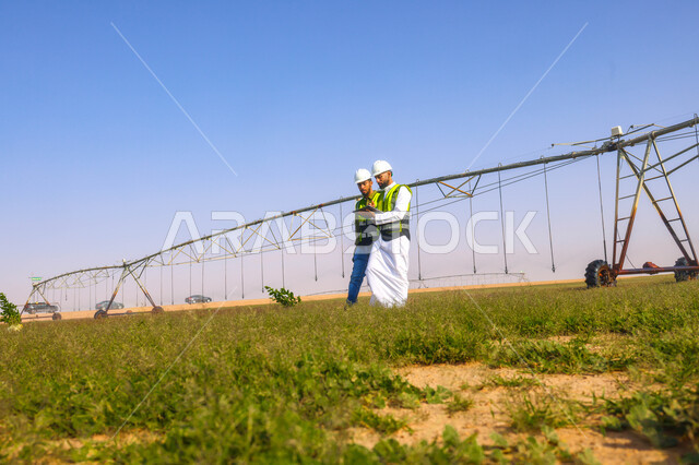 مهندسان زراعيان عربيان خليجيان سعوديان في حقل زراعي ، إرتداء خوذة وسترة الحماية، إتفاقيات و صفقات عمل، الاراضي والحقول الزراعية، آلات ومعدات الري المستقبلي، اذرع الري المحوري