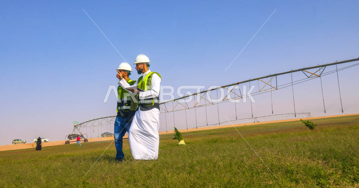 Two Saudi Arab Gulf agricultural engineers in an agricultural field, wearing a helmet and