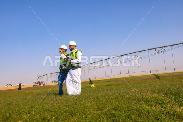 مهندسان زراعيان عربيان خليجيان سعوديان في حقل زراعي ، إرتداء خوذة وسترة الحماية، إتفاقيات و صفقات عمل، الاراضي والحقول الزراعية، آلات ومعدات الري المستقبلي، اذرع الري المحوري