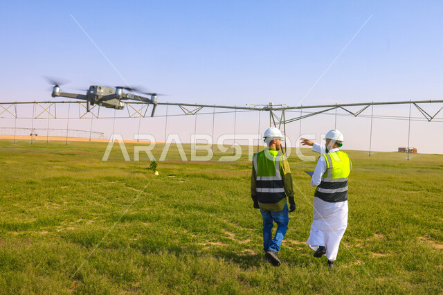 مهندسان زراعيان عربيان خليجيان سعوديان في حقل زراعي ، إرتداء خوذة وسترة الحماية، إتفاقيات و صفقات عمل، الاراضي والحقول الزراعية، آلات ومعدات الري المستقبلي، اذرع الري المحوري