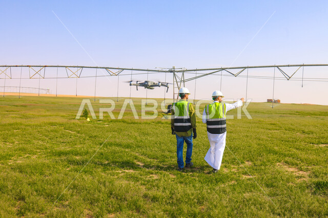 مهندسان زراعيان عربيان خليجيان سعوديان في حقل زراعي ، إرتداء خوذة وسترة الحماية، إتفاقيات و صفقات عمل، الاراضي والحقول الزراعية، آلات ومعدات الري المستقبلي، اذرع الري المحوري