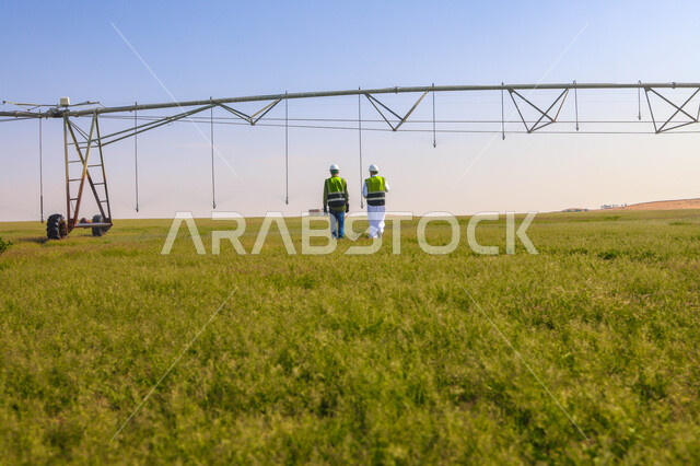 مهندسان زراعيان عربيان خليجيان سعوديان في حقل زراعي ، إرتداء خوذة وسترة الحماية، إتفاقيات و صفقات عمل، الاراضي والحقول الزراعية، آلات ومعدات الري المستقبلي، اذرع الري المحوري