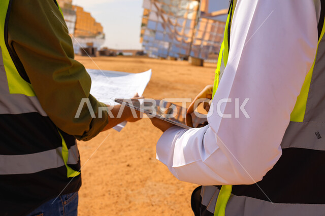 مهندسان عربيان خليجيان سعوديان يشرفان على محطات الطاقة الشمسية ، إرتداء خوذة وسترة الحماية ، الإشراف على العمل، ستلايت، أنظمة الطاقة الشمسية، الطاقة المتجددة، ألواح شمسيه 