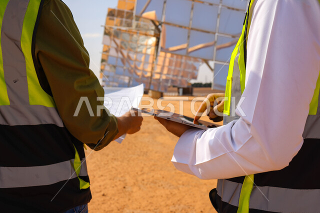 مهندسان عربيان خليجيان سعوديان يشرفان على محطات الطاقة الشمسية ، إرتداء خوذة وسترة الحماية ، الإشراف على العمل، ستلايت، أنظمة الطاقة الشمسية، الطاقة المتجددة، ألواح شمسيه 