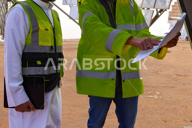 Two Saudi Arabian Gulf engineers supervising solar power plants, wearing a helmet and protection jacket, supervising work, satellite, solar energy systems, renewable energy, solar panels