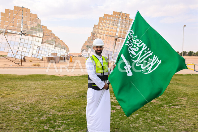 مهندس عربي خليجي سعودي يحمل علم المملكة، محطات الطاقة الشمسية، مستقبل الطاقة المتجددة، ألواح شمسية، اليوم الوطني السعودي 92، رؤية السعودية 2030