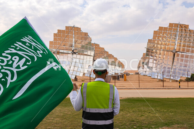 مهندس عربي خليجي سعودي يحمل علم المملكة، محطات الطاقة الشمسية، مستقبل الطاقة المتجددة، ألواح شمسية، اليوم الوطني السعودي 92، رؤية السعودية 2030