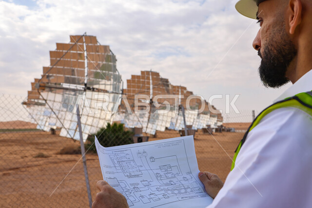 مهندس عربي خليجي سعودي، يرتدي الخوذة وسترة الحماية، يحمل بيده مخططات وتصاميم هندسية، التدقيق والإشراف على العمل، مفهوم هندسة الطاقة، مهن ووظائف سعودية، محطات الطاقة الشمسية، ألياف شمسية، ستلايت