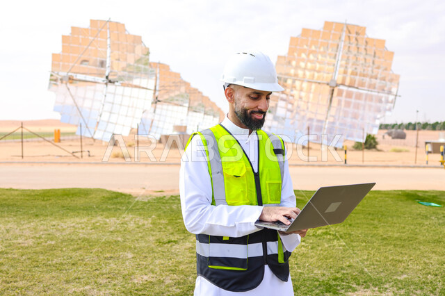 مهندس عربي خليجي سعودي، يرتدي الخوذة وسترة الحماية، يحمل بيده جهاز تقني، التدقيق والإشراف على العمل، مفهوم هندسة الطاقة، مهن ووظائف سعودية، محطات الطاقة الشمسية، ألياف شمسية، ستلايت