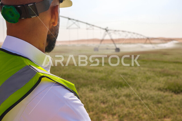 مهندس زراعي عربي خليجي سعودي يقف في حقل زراعي، إرتداء خوذة وسترة الحماية ، الإشراف على العمل, الات ومعدات الري المستقبلي، اذرع الري المحوري