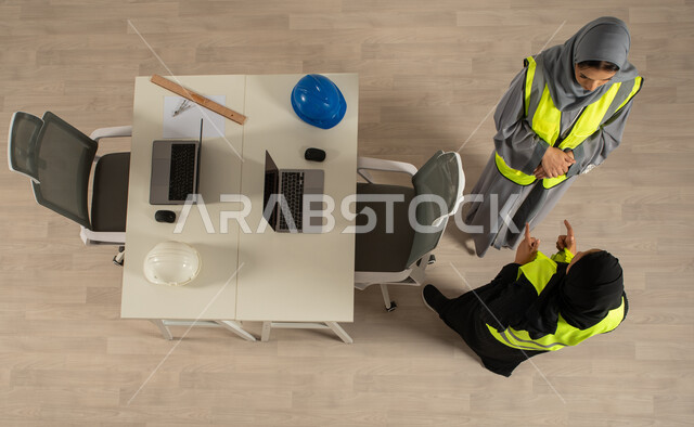 حوارات ونقاشات عمل، صورة عامودية علوية لمهندستان خليجيتان سعوديتان تتناقشان، مهنة الهندسة المعمارية، العمالة السعودية وفرص العمل، استخدام جهاز الحاسوب المحمول، ارتداء السترة الخاصة بالعمل، مهن ووظائف مكتبية سعودية