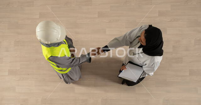 توقيع صفقات جديدة، اتفاقيات عمل ناجحة، صورة عامودية علوية لسيدتان عربيتان خليجيتان سعوديتان تتصافحان، مهنة الهندسة المعمارية، ارتداء ملابس العمل، العمالة السعودية وفرص العمل، مهنة الطب والرعاية الصحية، عمل جماعي مشترك، مهن ووظائف سعودية